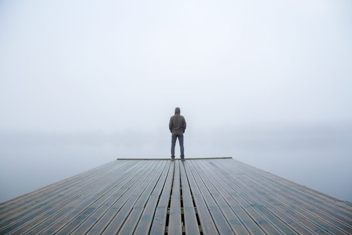 Depression und Burnout sind nicht trennscharf voneinander abgrenzbar. Mann steht alleine auf einen Steg im Nebel.